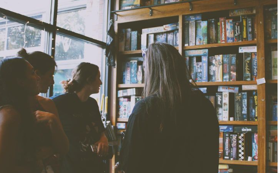 People inside The Rook & Pawn standing next to the bookshelf.