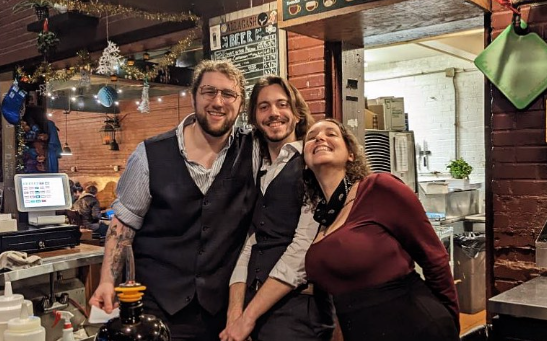 Three people standing inside The Rook & Pawn.