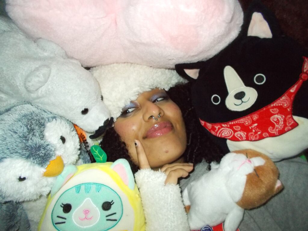 Hannah laying in a pile of stuffed animals wearing the fluffy beanie.