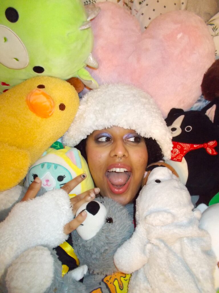 Hannah in a pile of stuffed animals wearing the fluffy beanie. 