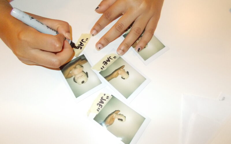 Hannah labeling polaroids of stuffed animal with crochet hat.