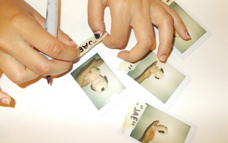 Hannah labeling polaroids of stuffed animal with crochet hat.
