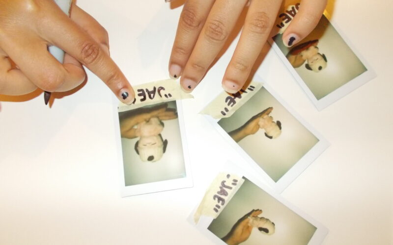 Hannah labeling polaroids of stuffed animal with crochet hat.