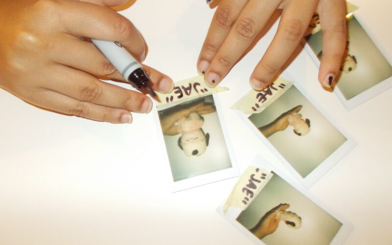 Hannah labeling polaroids of stuffed animal with crochet hat.