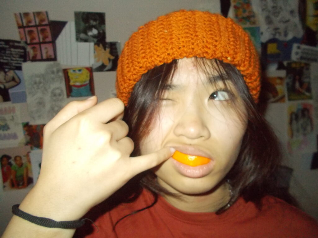 Amanda with an orange peel grill and the beanie. The wall behind her is covered in posters.