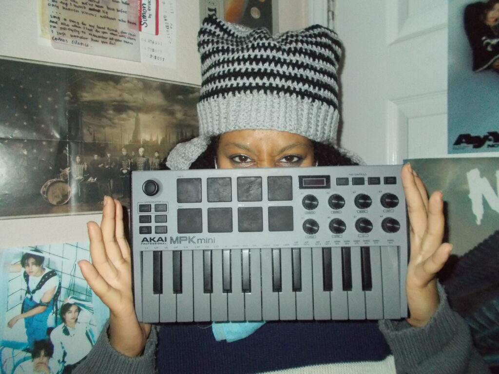 Hannah wearing the star beanie and holding a mini keyboard. The wall behind her is covered in posters.