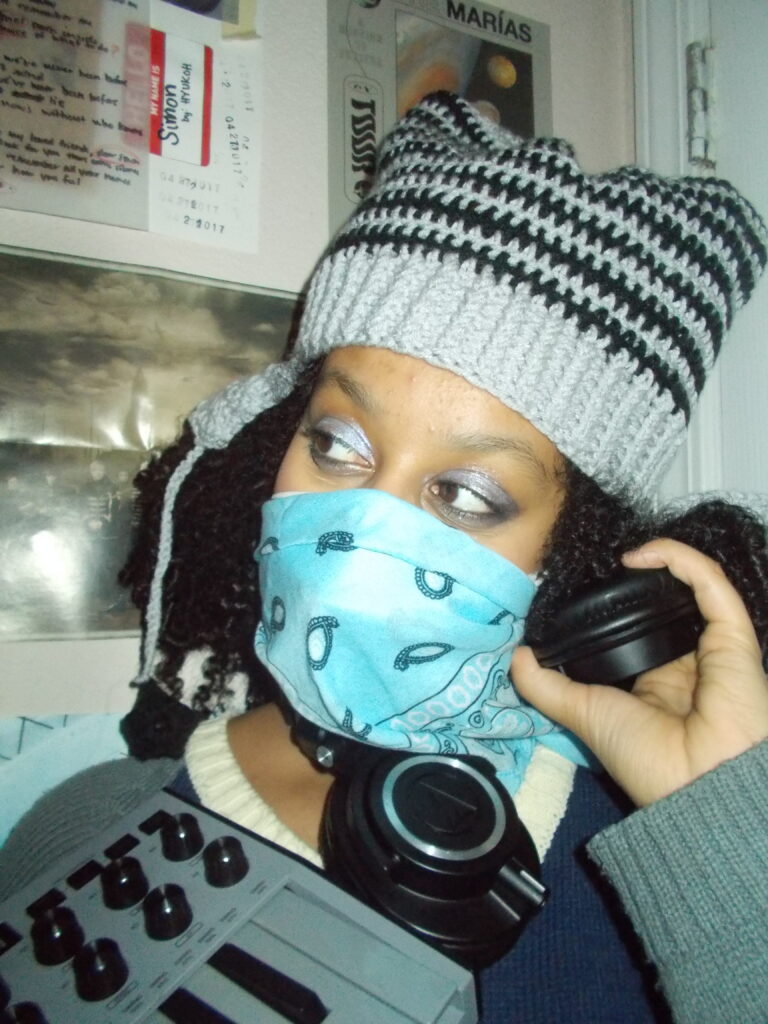 Hannah wearing the star beanie and a blue bandana. She's holding a mini keyboard and wearing headphones.