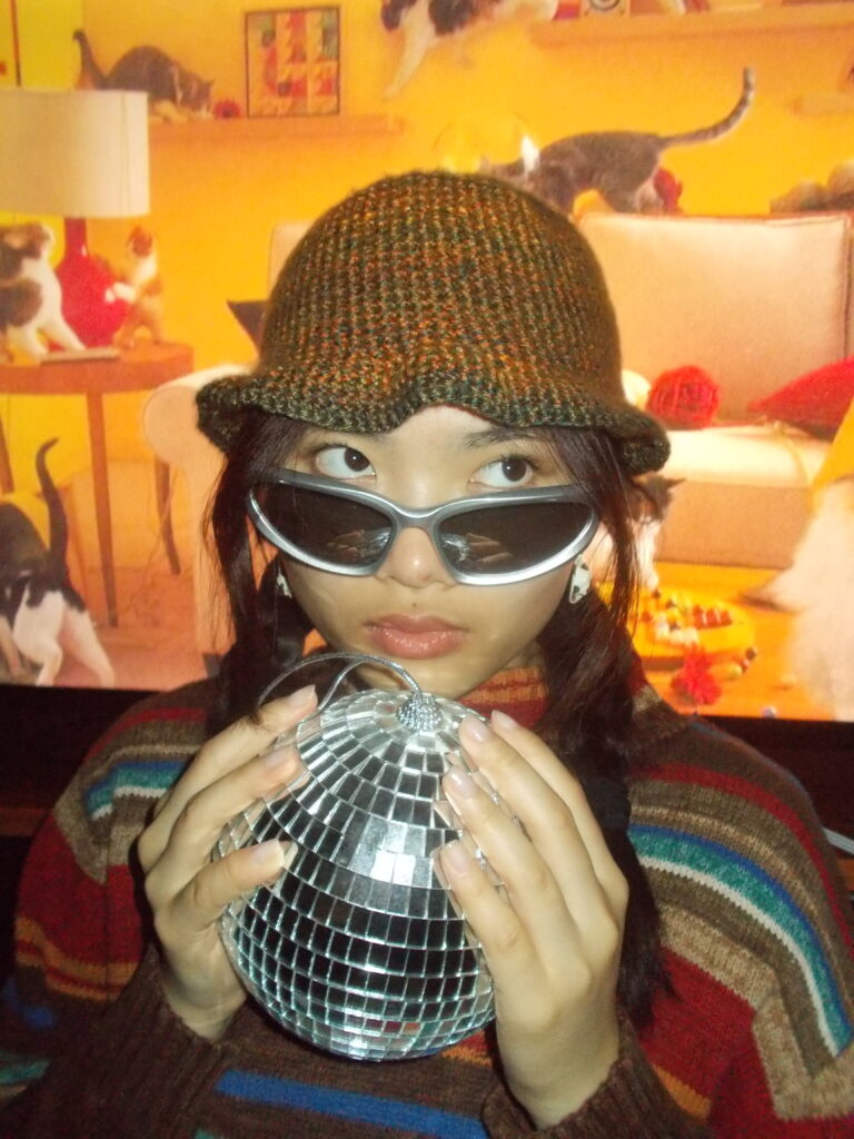Amanda wearing the bucket hat, a striped shirt, and sunglasses. She's holding a disco ball between her palms.